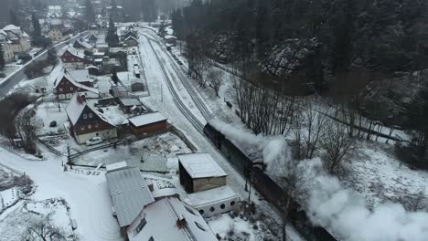 Drone-Shot-of-an-old-steam-locomotive-arriving-at-a-small-station-in-a-German-village-in-a-winter-landscape