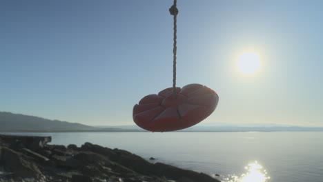 Rope-swing-moving-gently-against-early-morning-autumn-sun-reflecting-gently-off-the-sea
