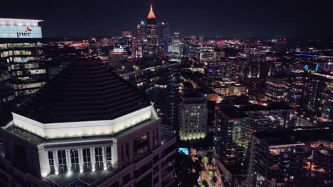 Toma-Aérea-Hacia-Atrás-Sobre-La-Iluminación-Del-Paisaje-Urbano-De-Atlanta-Por-La-Noche-En-Georgia---Torre-PWC-Y-Bank-Of-America-Plaza-Al-Fondo