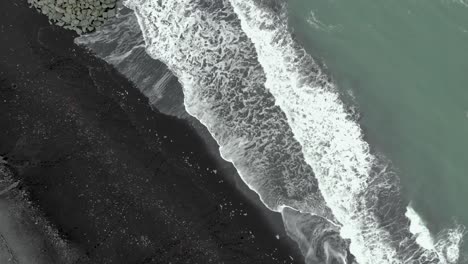 Von-Oben-Nach-Unten-Schwenkende-Luftaufnahme-Des-Diamond-Beach-In-Island,-Wo-Wellen-Eis-Auf-Den-Schwarzen-Sand-Legen