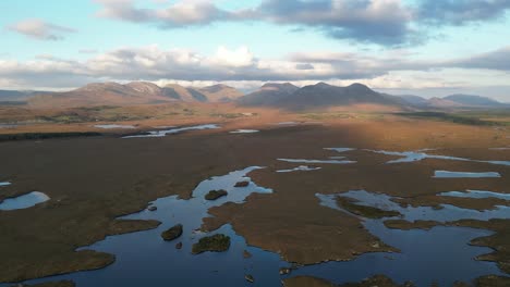 Wide-aerial-shot-of-Connemara-Lakes-with-calm-lakes-in-the-foreground-and-Beanna-Beola-mountain-range-in-the-distance,-slowly-revealing-aerial-shot