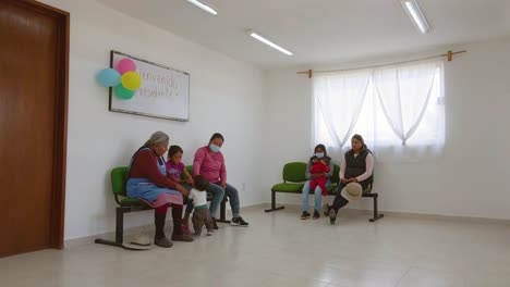Varias-Mujeres-Con-Máscaras-Y-Niños-Esperan-Afuera-De-Una-Hermosa-Clínica-Adornada-Con-Globos-De-Colores-En-Ecatepec-De-Morelos,-México.