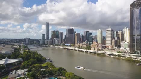 Ferry-crosses-Brisbane-river-as-clouds-cast-dark-shadows-on-city-skyline,-Australia