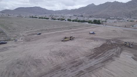 A-drone-gracefully-circles-an-elevating-scraper-parked-in-the-middle-of-a-lot-on-a-prospective-home-construction-site,-offering-a-glimpse-of-other-heavy-machinery-diligently-at-work
