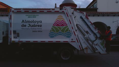 In-Ecatepec-de-Morelos,-Mexico,-a-municipal-employee-is-utilizing-the-garbage-truck-to-collect-waste-throughout-the-town