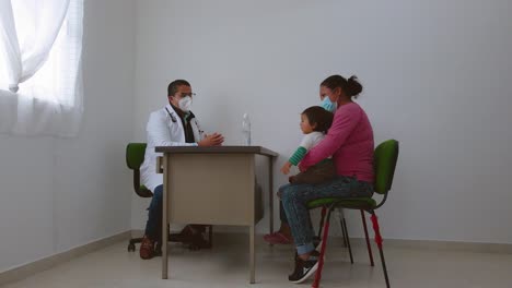 At-an-astonishing-clinic,-a-doctor-is-giving-guidance-to-a-woman-and-her-children,-and-there-is-a-table-with-a-sanitizer-bottle-on-it
