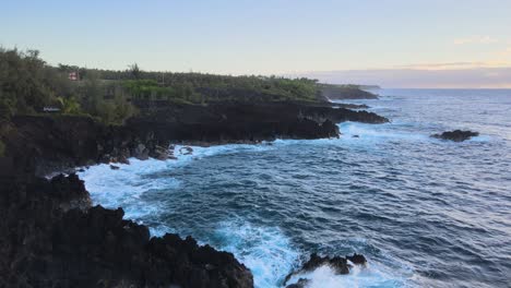 Gently-gliding-above,-a-drone-captures-the-raw-beauty-of-rugged-rocks-being-embraced-by-deep-blue-waves-on-the-enchanting-shores-of-Big-Island,-Hawaii