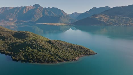 Pigeon-island-in-calm-lake-Wakatipu-surrounded-by-scenic-mountains,-aerial