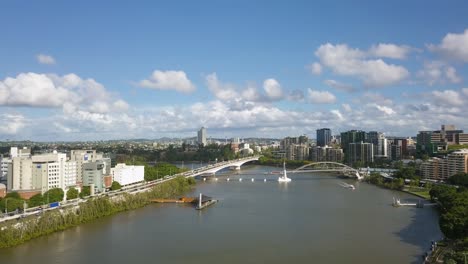 Aerial-dolly-over-Brisbane-river-as-cars-drive-along-bridge-at-midday,-skyline-view