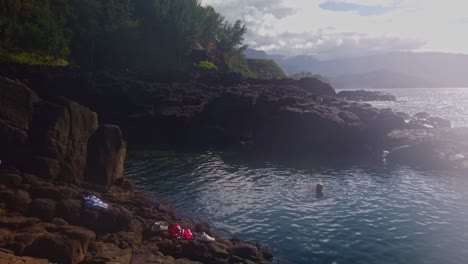Gimbal-wide-panning-shot-of-people-swimming-in-Queen's-Bath-among-ancient-lava-rocks-on-the-north-shore-of-Kaua'i-in-Hawai'i