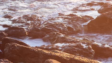 Waves-splashing-against-the-rocky-coastline-close-up-static-shot,-with-a-sunflare