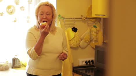 Senior-woman-eating-apple-in-the-yellow-kitchen
