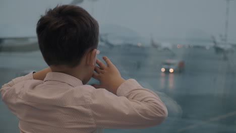 Boy-waiting-for-the-flight-and-looking-at-airplanes-outside