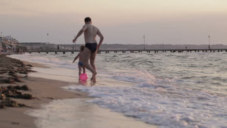 Father-and-son-running-along-the-beach-with-ball