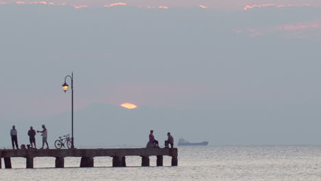 People-relaxing-on-a-pier-at-sunset-Ship-is-passing-by