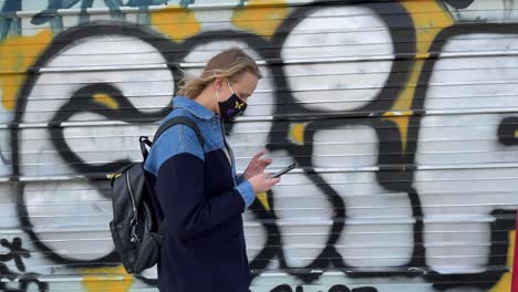 Frau-In-Maske-Mit-Handy-Vor-Schmuddeligen-Graffitiwänden