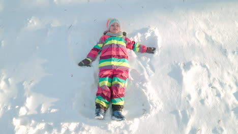 Kleines-Mädchen-Macht-Schneeengel-An-Einem-Sonnigen-Wintertag