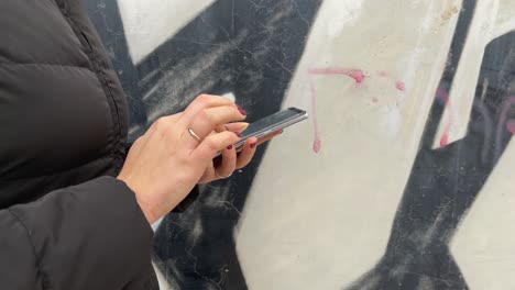 Woman-in-a-hurry-and-using-mobile-on-the-go-view-against-graffiti-walls