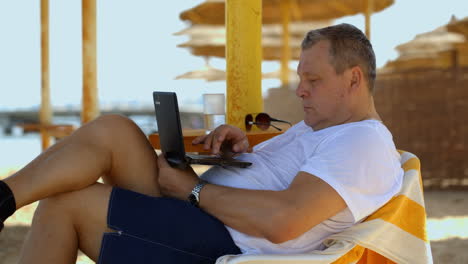 Hombre-Relajándose-Con-Una-Computadora-Portátil-En-El-Resort-De-Playa