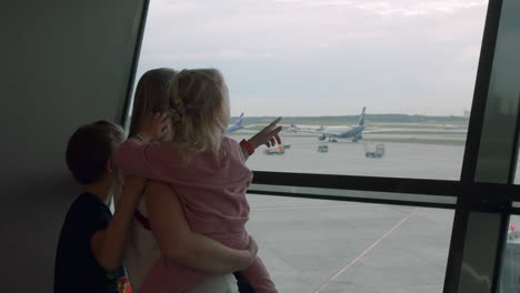 Madre-Con-Niños-Curiosos-Esperando-El-Vuelo-En-El-Aeropuerto.