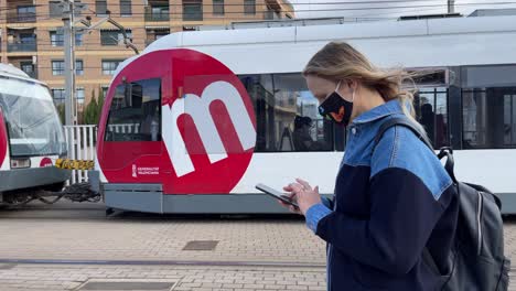 Woman-citizen-with-mobile-walking-in-the-street-with-tram-passing-by