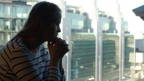 Sad-woman-being-deep-in-thoughts-and-then-looking-out-the-window-with-city-view