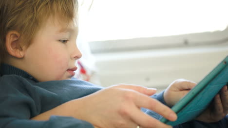 Boy-in-the-train-using-touchpad-held-by-mother