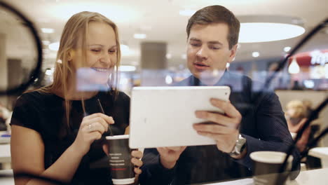 Man-and-woman-in-cafe-talking-vividly-about-something-shown-on-pad