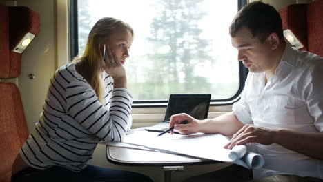 Hombre-Y-Mujer-Discutiendo-Dibujo-Durante-Un-Viaje-De-Negocios-En-El-Tren