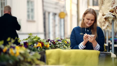 Mujer-Usando-Su-Teléfono-Inteligente-Sentada-En-Un-Café-Al-Aire-Libre