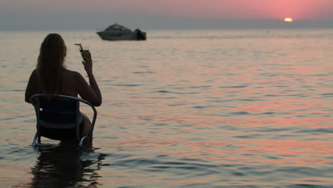 Frau-Mit-Cocktail-Sitzt-Auf-Einem-Stuhl-Im-Meer