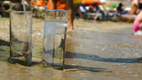 Pouring-water-into-two-glasses-on-beach