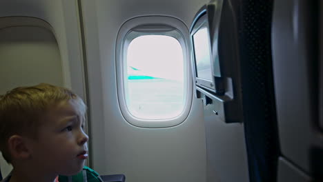 Kleiner-Junge-Berührt-Sitzmonitor-Im-Flugzeug