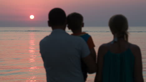 Familia-De-Tres-Personas-Viendo-La-Puesta-De-Sol-Sobre-El-Mar