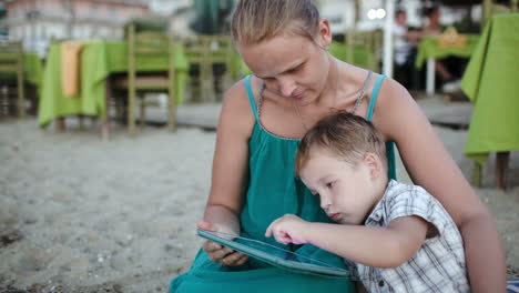 Madre-E-Hijo-Usando-Tablet-Pc-Cerca-Del-Café-De-La-Playa