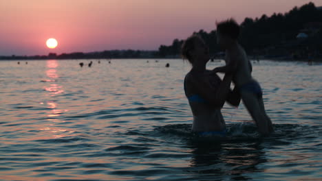 Mother-throwing-son-in-sea-at-sunset