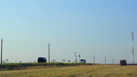 Cars-going-by-field-with-hay-roll-in-countryside