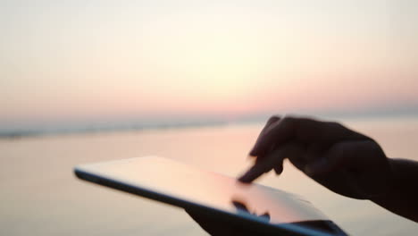 Female-hands-typing-on-tablet-PC-by-sea-at-sunset