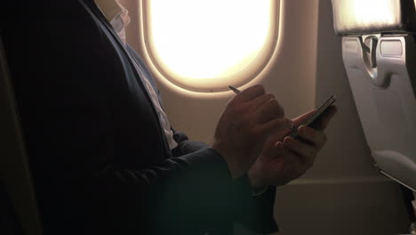 Hombre-Usando-Un-Bolígrafo-Para-Escribir-En-Un-Teléfono-Inteligente-En-Un-Avión