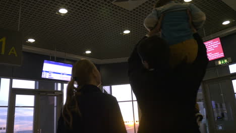 Family-at-airport-terminal-looking-outside-at-sunset