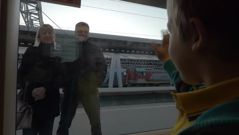 Zeitlupe-In-Sankt-Petersburg,-Russland.-Kleiner-Junge-Winkt-Aus-Dem-Zugfenster-Den-Großeltern-Zu,-Die-Auf-Dem-Bahnsteig-Stehen