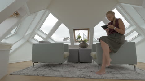 View-of-young-blond-woman-sitting-on-the-side-of-arm-chairs-using-tablet-inside-of-room-in-a-Cube-house-Rotterdam-Netherlands