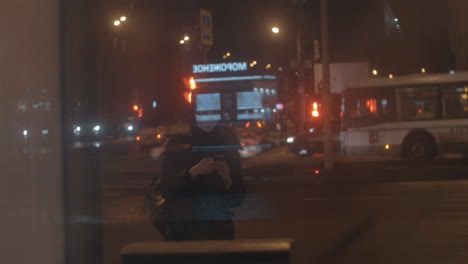 Mujer-Con-Celular-En-La-Parada-De-Autobús-En-La-Ciudad-De-Noche