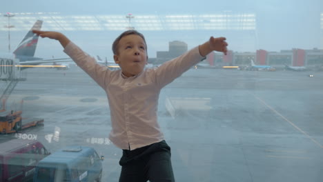 Child-showing-flying-bird-against-window-with-airport-area-view