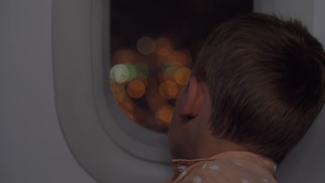 Niño-Viajando-En-Avión-Por-La-Noche-Y-Mirando-Iluminador