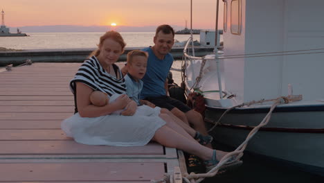 Eltern-Mit-älterem-Sohn-Und-Baby-Sitzen-Bei-Sonnenuntergang-Auf-Dem-Pier