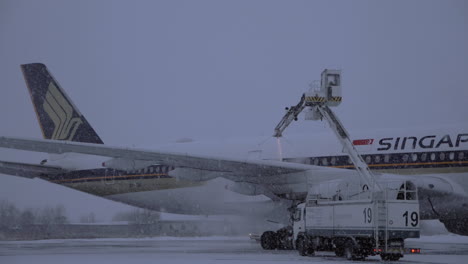 Spraying-de-icing-fluid-on-the-plane-of-Singapore-Airlines-in-snowy-evening