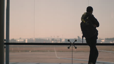 Una-Vista-Trasera-De-Un-Hombre-Parado-Junto-A-Una-Enorme-Ventana-Del-Aeropuerto.