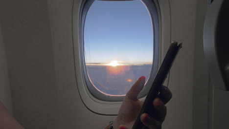 Nutzung-Des-Mobiltelefons-Im-Flugzeugfenster-Mit-Sonnenaufgang-Im-Hintergrund