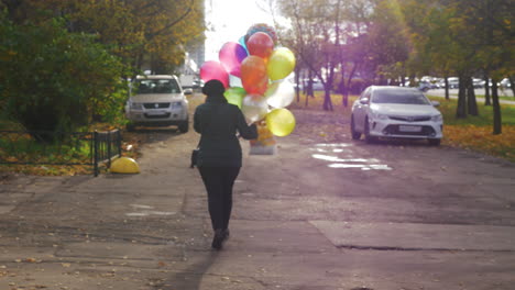 Eine-Zeitlupe-Einer-Frau,-Die-Mit-Bunten-Luftballons-Die-Straße-Entlang-Läuft